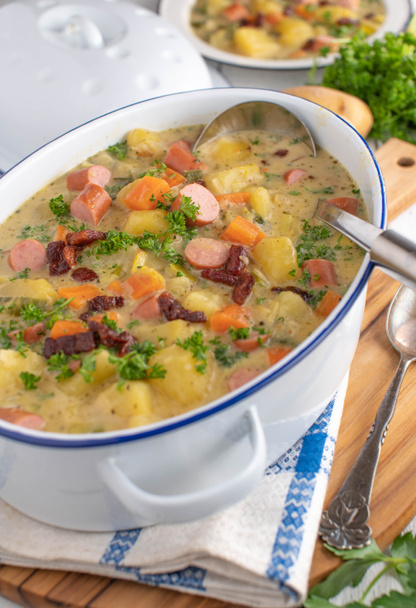 Горшок с домашним картофельным супом или картофельным рагу с хрустящим беконом и венской колбасой. Подается в деревенском горшке на кухонном столе - Фото, изображение
