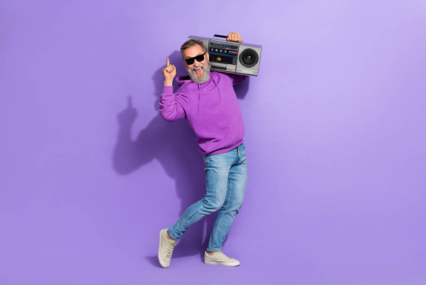 Photo of old carefree funny positive man purple hoodie hold boombox finger directing up at empty space isolated on violet color background. - Foto, Imagen