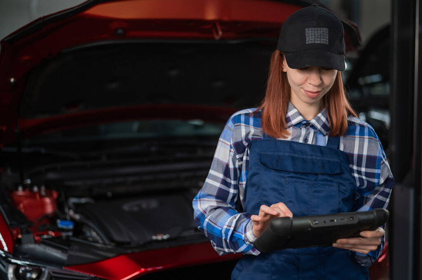 Caucasian female auto mechanic uses a special computer to diagnose faults - 写真・画像