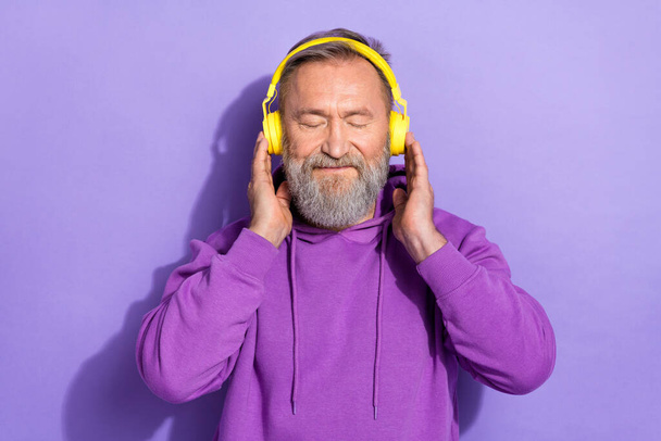Portrait of old positive good mood man dressed purple hoodie touch headphones eyes closed enjoy music isolated on violet color background. - Фото, зображення