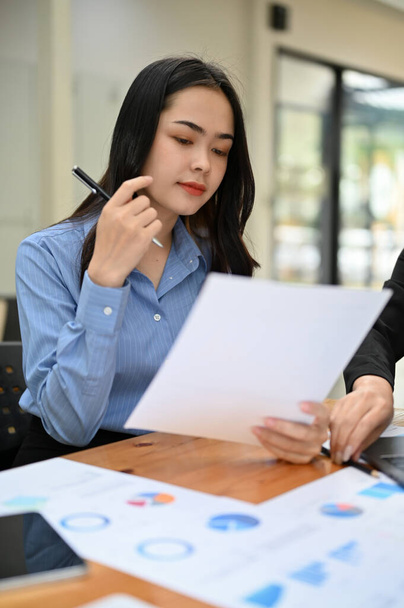 Portrait, Young Asian businesswoman or female financial worker brainstorming and analyzing financial data on the report with her team. - Photo, Image