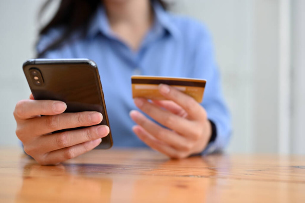Крупный план, женщина сидит за столом, держит смартфон и кредитку. мобильные платежи, интернет-банкинг, безналичное общество - Фото, изображение
