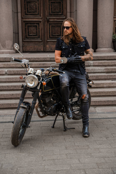 ロッカーのように見える流行の男のショットと彼の古いファッションオートバイ. - 写真・画像