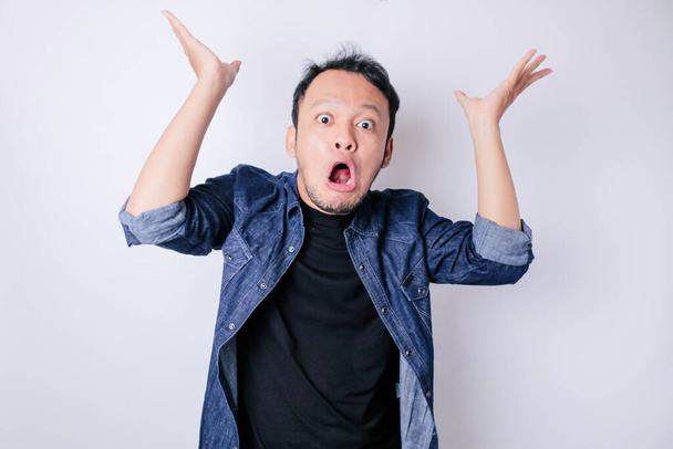 Shocked Asian man wearing blue navy shirt pointing at the copy space on top of him, isolated by white background - 写真・画像