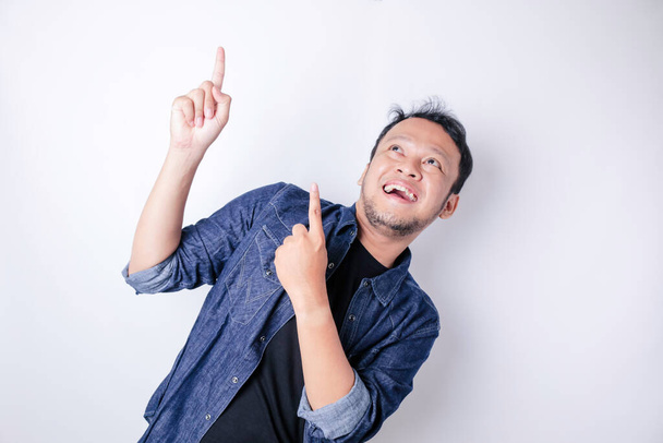 Smiling handsome Asian man pointing finger up to empty space isolated white background - Foto, imagen