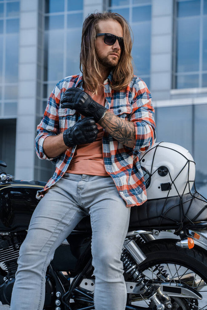 Portrait of urban biker with long hairs dressed in stylish casual attire outdoors. - Foto, Imagen