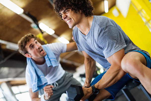 Fitness, sport, exercising and diet concept. Happy fit man exercising together with his personal trainer, friend in gym. - 写真・画像