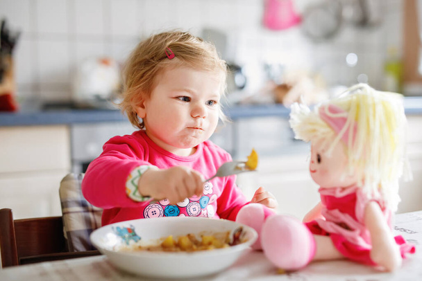 Adorable baby girl eating from fork vegetables and pasta. food, child, feeding and development concept. Cute toddler, daughter with spoon sitting in highchair and learning to eat by itself - Photo, Image