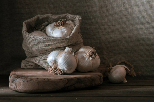 big Garlic Cloves and Bulb wooden table cooking on dark background. burlap sack cutting board copy space Close-up  rustic  still life spice Healthy organic antioxidant raw - Foto, Imagem