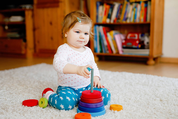 Адекватная симпатичная маленькая девочка, играющая с учебными деревянными игрушками дома или в детском саду. Туфелька с разноцветной стопкой пирамид и музыкальной игрушкой. Счастливый здоровый ребенок веселится с разными игрушками. - Фото, изображение