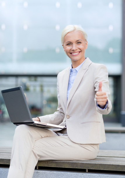 smiling businesswoman working with laptop outdoors - Foto, afbeelding