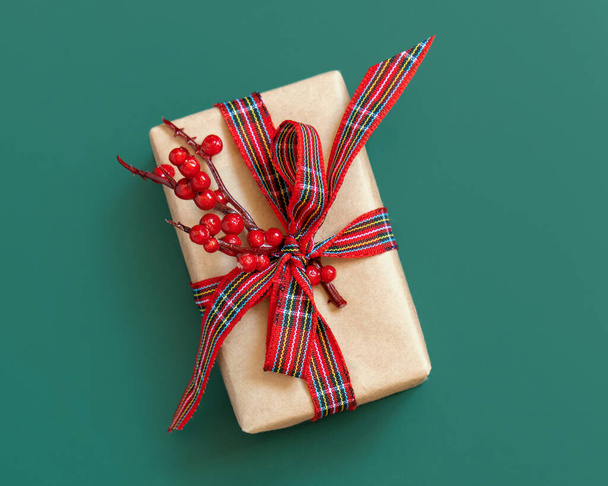 Confezione regalo avvolta in carta kart con fiocco a nastro rosso e bacche in vista verde dall'alto. Natale o Capodanno Atmosfera di vacanza lay flat - Foto, immagini