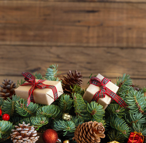 Scatole regalo avvolte su rami di abete reen vicino a decorazioni natalizie e pigne da vicino su sfondo di legno, copia lo spazio. Natale o Capodanno Atmosfera natalizia  - Foto, immagini