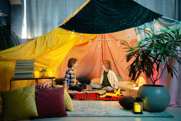 Two young cute boys are playing inside a nice comfy tent that has a hippie vibe to it, the tent is an indoor one. - Fotó, kép