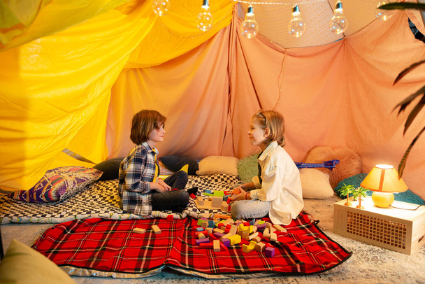A close up shot of two youthfull buddies playing with airplanes and one of them drops it on the duvet all while being in a massive indoor blanket tent. Portrait - Foto, afbeelding