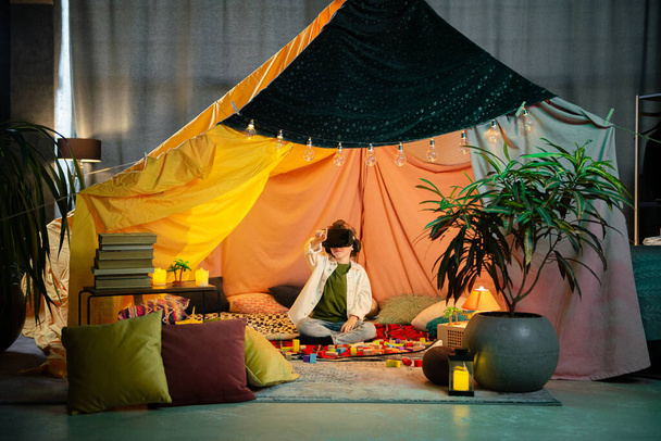 The boy chilling together inside a blanket fort while playing with a virtual reality headset and laughing. - Foto, Imagem