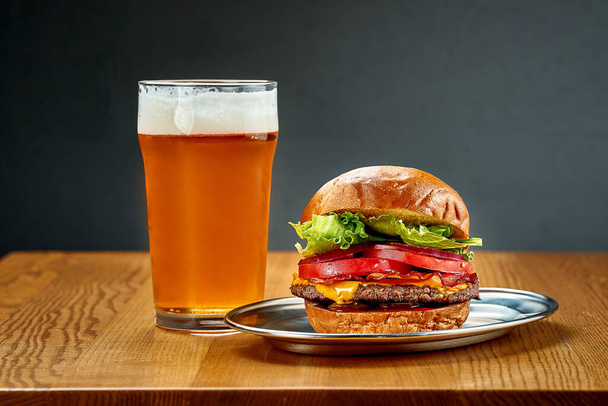 A big juicy burger with vegetables and a glass of beer. Close-up, selective focus - Fotó, kép