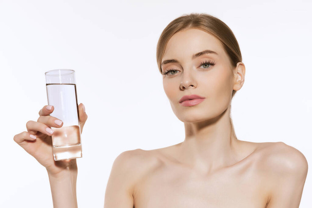 Keep water balance. Charming pretty young woman with light makeup holding glass of pure water and looking at camera isolated over white background. Concept of beauty, skincare, cosmetology, spa - Фото, зображення