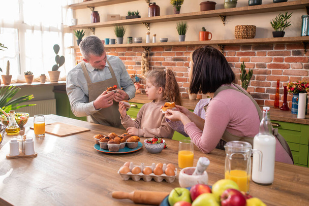 Very charismatic and amazing looking family members talking some strawberry at the kitchen island in the morning taking healthy breakfast. - Фото, зображення