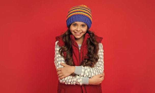 winter fashion. pretty happy kid with curly hair in hat. female fashion model. teen girl in down vest. portrait of child wearing warm clothes. express positive emotion. - Fotografie, Obrázek