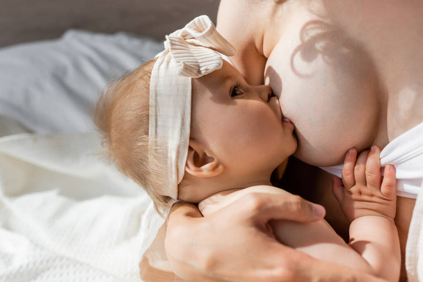 woman breastfeeding infant daughter in headband with bow  - Photo, Image