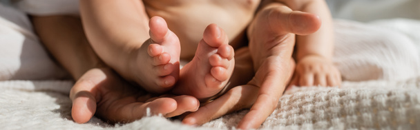 Ausgeschnittene Ansicht der Mutter mit winzigen nackten Füßen der kleinen Tochter in den Händen im Schlafzimmer, Banner - Foto, Bild