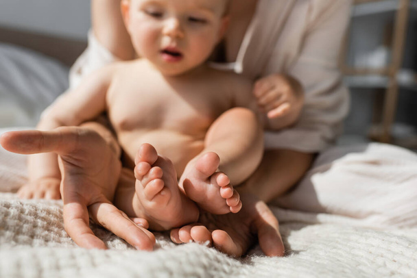 Mutter hält winzige nackte Füße der kleinen Tochter im Schlafzimmer in Händen  - Foto, Bild