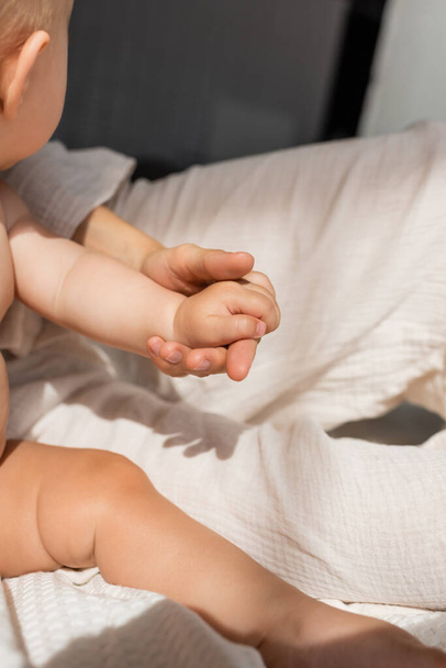 cropped view of mother holding hands with cute baby girl in bedroom  - Foto, Bild