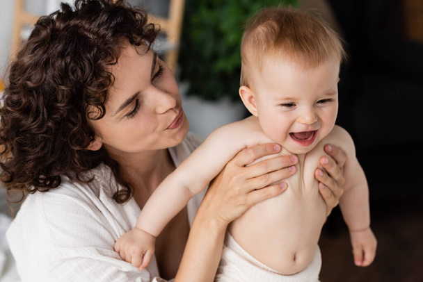 nő göndör haj gazdaság karok izgatott csecsemő baba nyitott szájjal - Fotó, kép