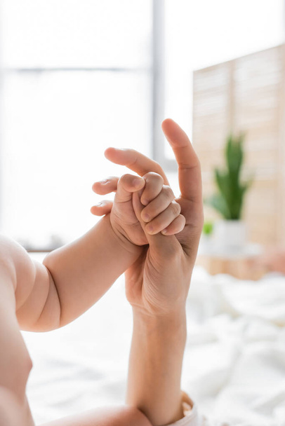 Cropped view of child holding finger of mother in blurred bedroom  - Photo, image