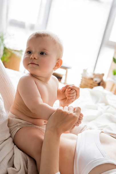 Woman holding hands of baby daughter on bed in morning  - Foto, Bild