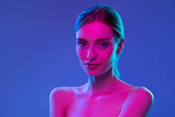 Inspiration. Young beautiful fashion model with well-kept skin and naked shoulders isolated over dark background in pink neon light. Vivid style, beauty, art, future concept. - Fotografie, Obrázek