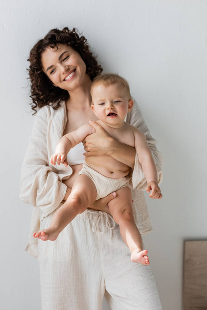 Happy woman in pajamas holding baby girl at home  - Valokuva, kuva