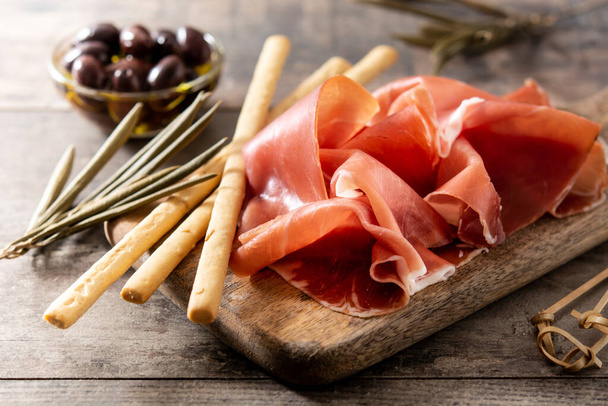 Spanish serrano ham with olives and breadstick on wooden table background - Фото, зображення