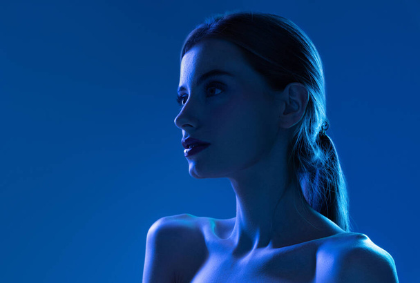 Portrait of female fashion model in neon light on blue gradient studio background. Beautiful caucasian girl with trendy make-up and well-kept skin. Vivid style, beauty, cosmetics concept. - Fotografie, Obrázek