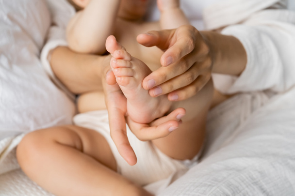 Cropped view of mother touching foot of baby daughter on bed  - Фото, зображення