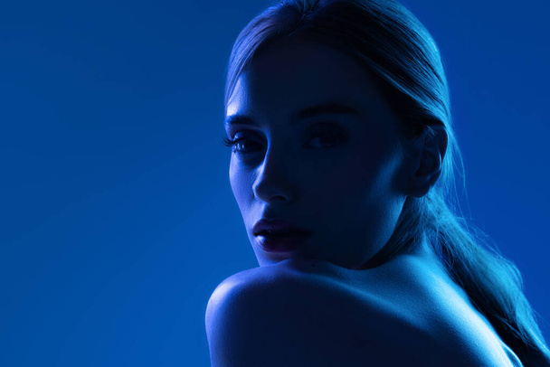 Portrait of female fashion model in neon light on blue gradient studio background. Beautiful caucasian girl with trendy make-up and well-kept skin. Vivid style, beauty, cosmetics concept. - Fotoğraf, Görsel