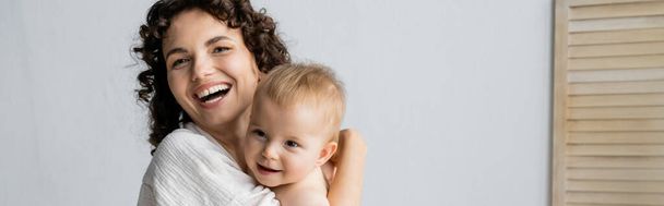 Cheerful woman hugging baby daughter at home, banner  - Photo, Image