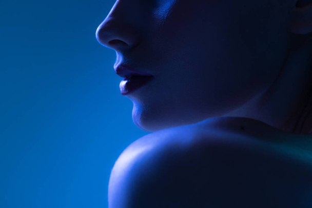 Night life. Cropped image of young woman in neon light on dark blue background. Monochrome. Cyberpunk style, beauty, cosmetics concept. Serious and thoughtful - 写真・画像