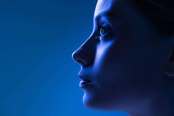 Closeup profile view of young pretty girl with well-kept skin isolated over dark blue background in neon light. Concept of high fashion, emotions, style, inspiration. Art portrait - Photo, image
