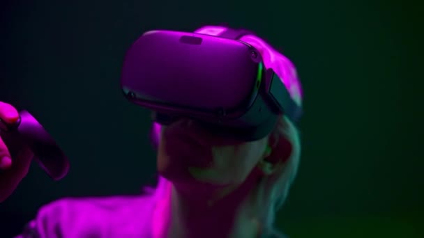 Impressed man experiencing VR headset videogame on neon background. Excited gamer using gadget for virtual reality. Male person in futuristic goggles playing controllers. Future technology concept  - Video