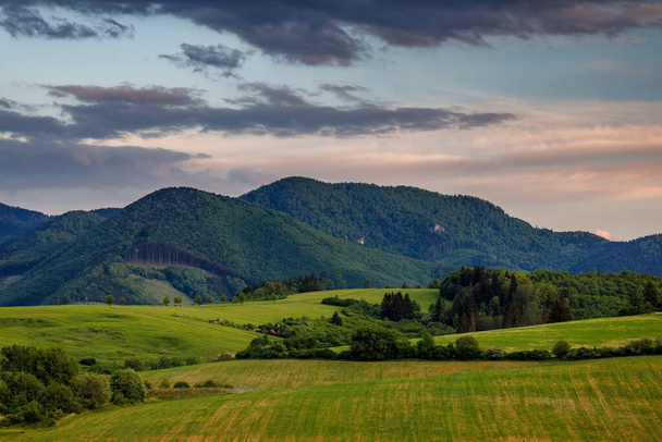 Wiosna wiejski krajobraz z dramatycznym niebem o zachodzie słońca. Łąki na zboczu Gór Małej Fatry na Słowacji, Europa. - Zdjęcie, obraz