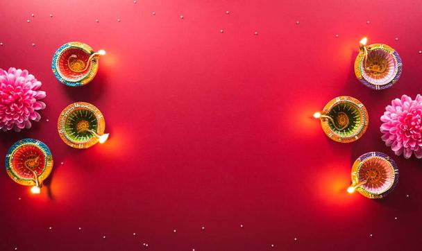 Happy Diwali - Clay Diya lamps lit during Diwali, Hindu festival of lights celebration. Colorful traditional oil lamp diya on red background - Fotografie, Obrázek