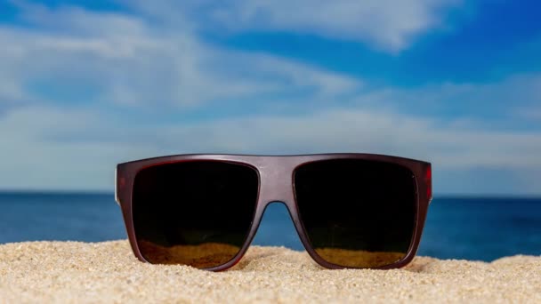 Ένα ζευγάρι γυαλιά ηλίου στην παραλία με περαστικά σύννεφα  - Πλάνα, βίντεο