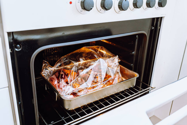 Vlees koken in plastic zak voor het bakken. Geen plastic concept. Vers schapenvlees of rundvlees verpakt in gekruide mouw klaar om te bakken, gezien door open ovendeur. Feestelijk diner, gezond eten zonder plantaardig vet en bakken - Foto, afbeelding