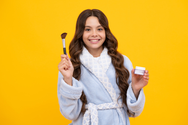 Beauty, make up and kids cosmetics. Teenage girl with brush applying blush to face isolated on yellow studio background - Fotografie, Obrázek