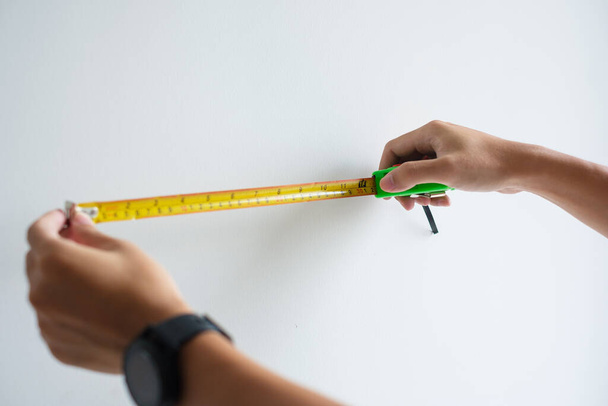 Рука человека с помощью ручной ленты для измерения с фоном стены в домашних условиях. DIY, дизайн интерьера, ремонт и улучшение концепции дома или квартиры - Фото, изображение