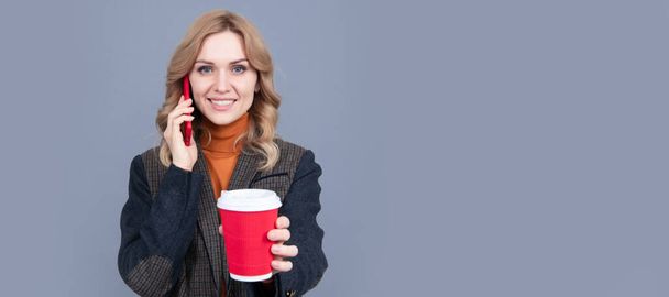 Happy woman talk on mobile phone giving hot cup grey background, tea. Woman portrait, isolated header banner with copy space - Photo, Image
