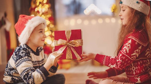 Boy giving red present box to cute girl. Concept of the Christmas and New Year holidays. - Фото, изображение