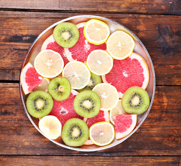 Ripe slices lemon, kiwi and grapefruit on tray on wooden background - 写真・画像
